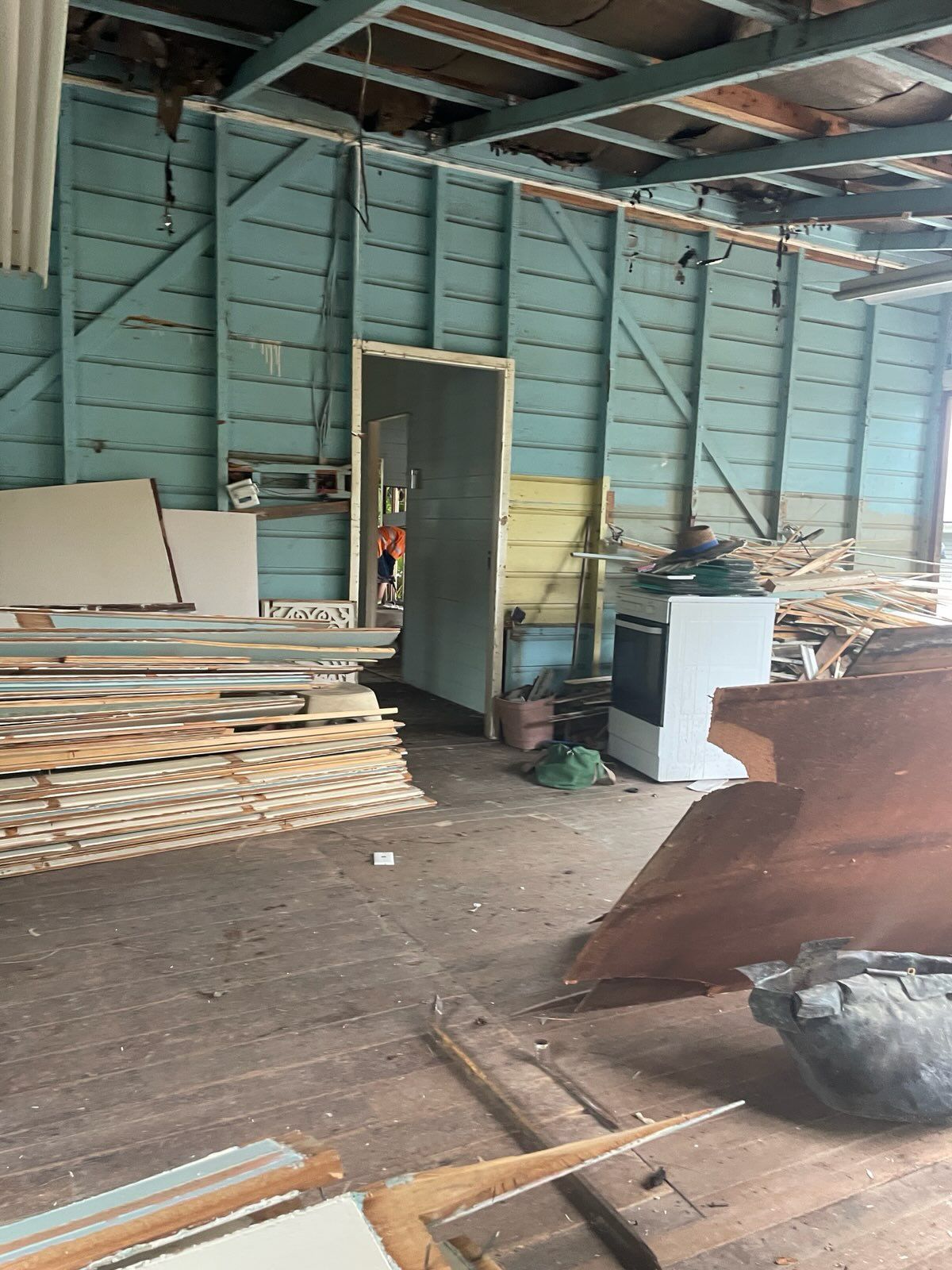 Inside an unfinished room with blue walls and wood flooring. Construction materials and an open doorway are visible.