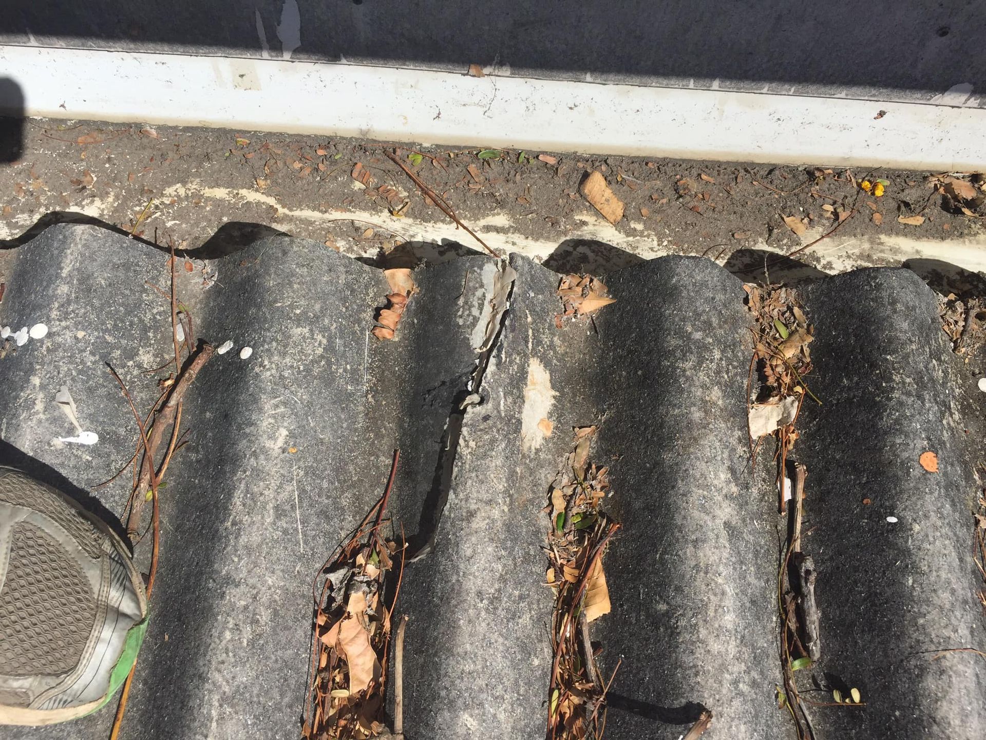 Damaged corrugated roof with debris and cracked panels.
