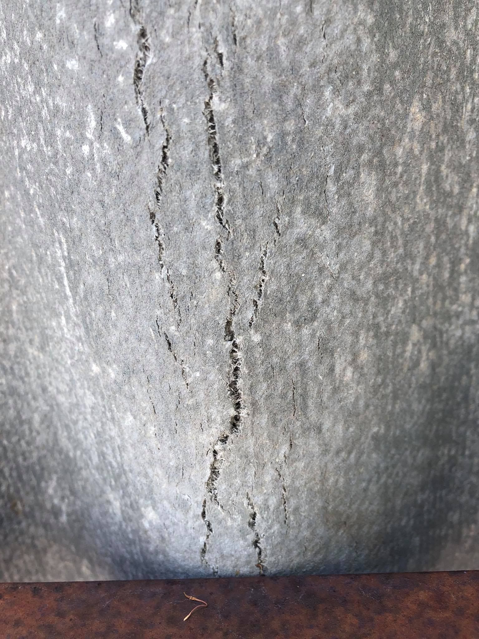 Cracked, textured gray metal surface with dark, vertical lines.
