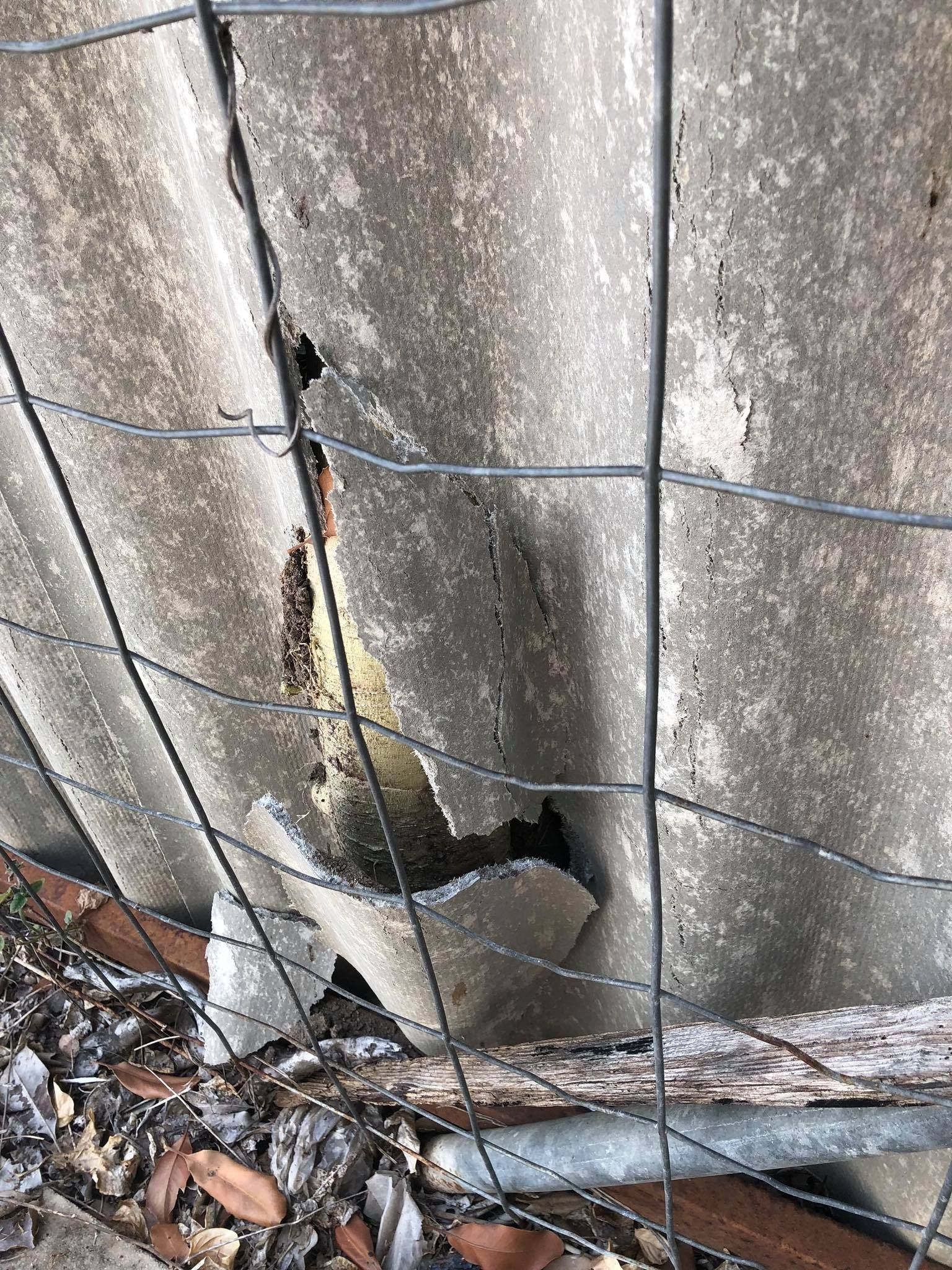 Damaged corrugated asbestos fence behind a wire fence.