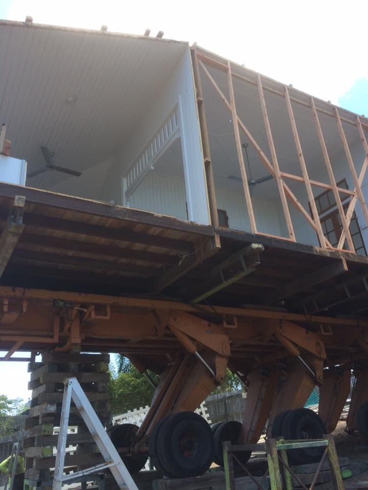 Ladder next to elevated machinery on wooden supports, wheels visible. Worker in vest.