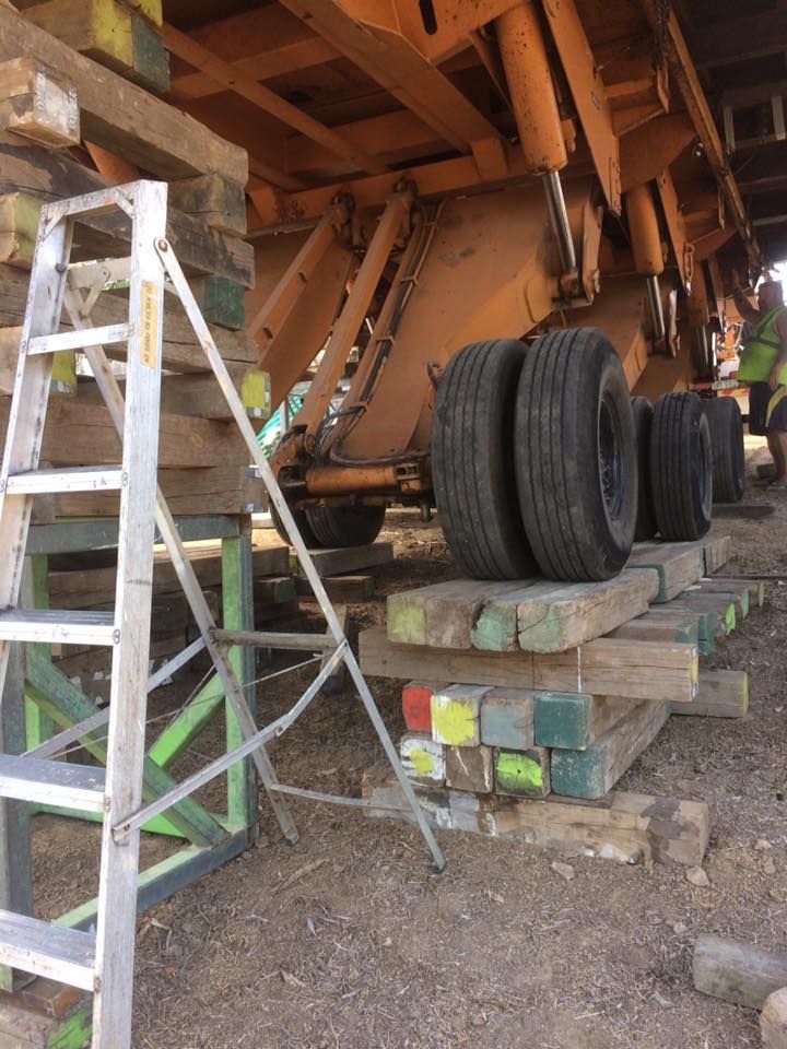 Ladder next to elevated machinery on wooden supports, wheels visible. Worker in vest.