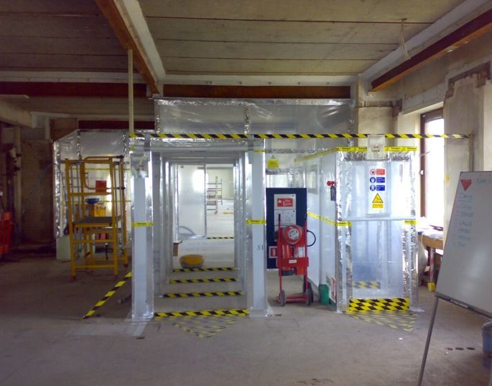Person in white protective suit, mask, and apron stands outside a garage under a bright sky.