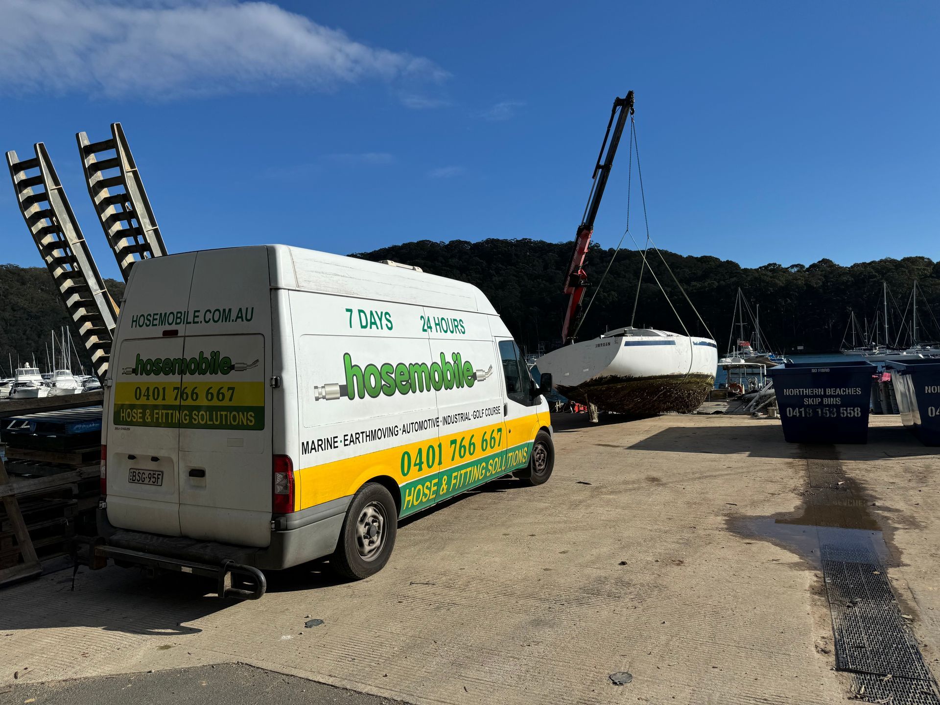 A white van is parked in a parking lot next to a boat being lifted by a crane. — Hosemobile In Kariong, NSW