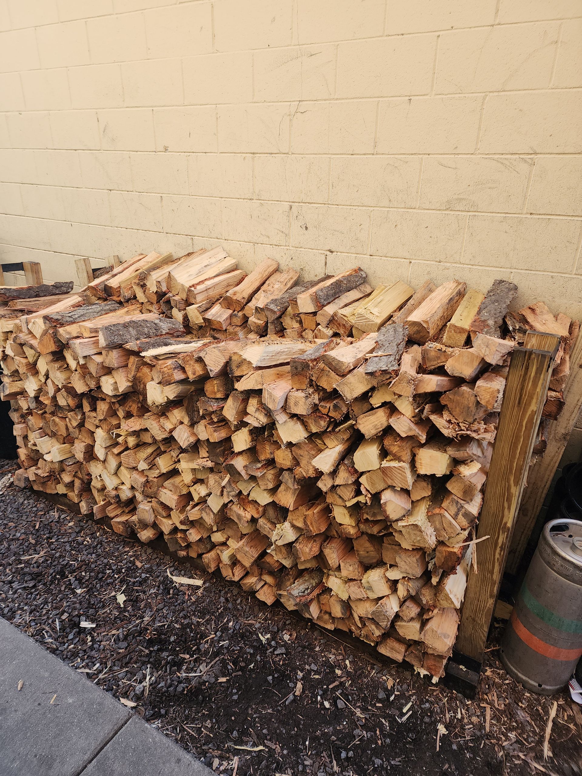 A large pile of wood is sitting in front of a brick wall.