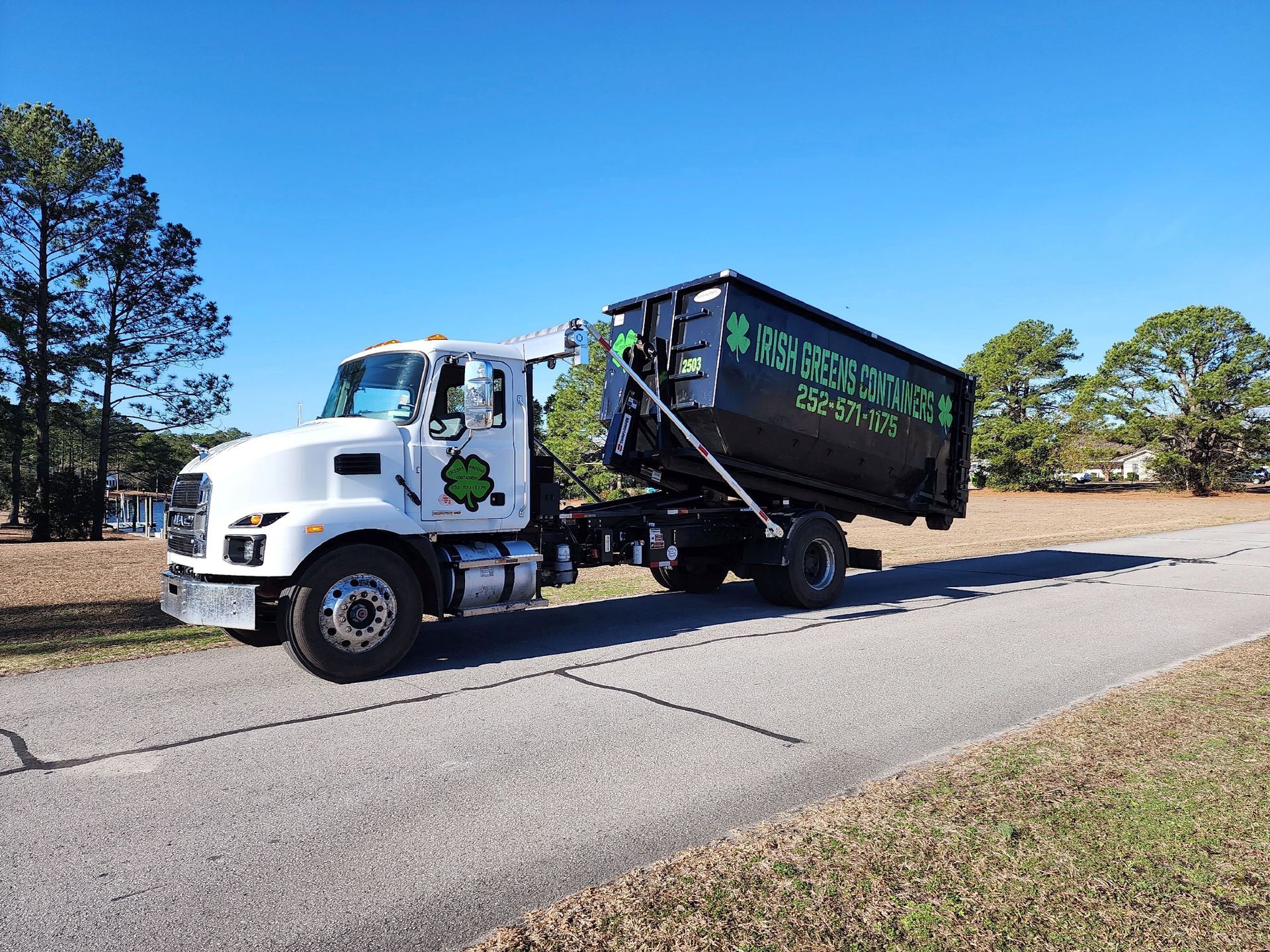 A dump truck is driving down a road with trees in the background.