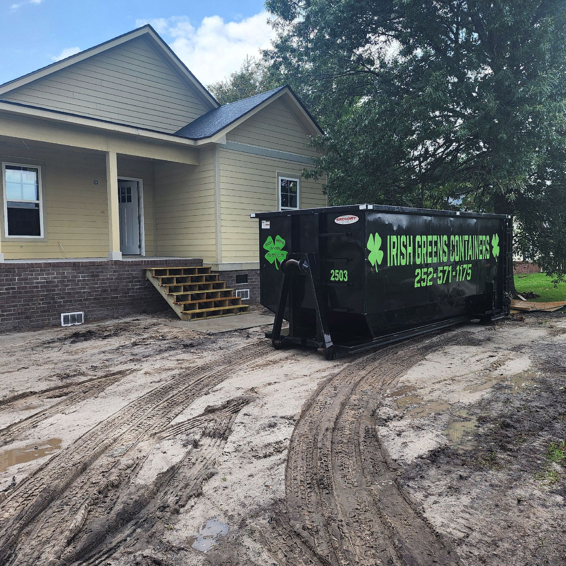 A black dumpster with a clover on it is parked in front of a house