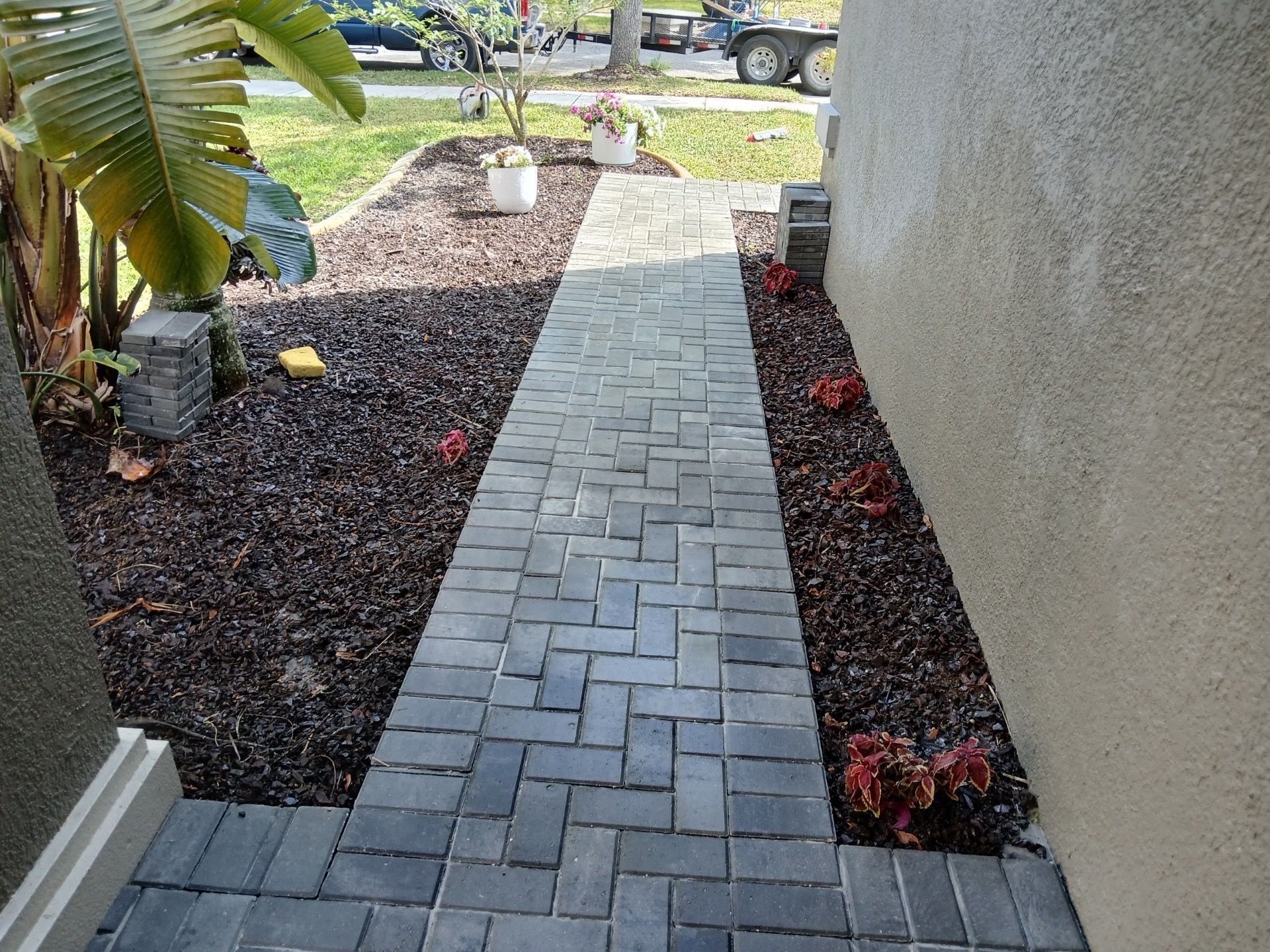 A brick walkway leading to a house with plants on the side