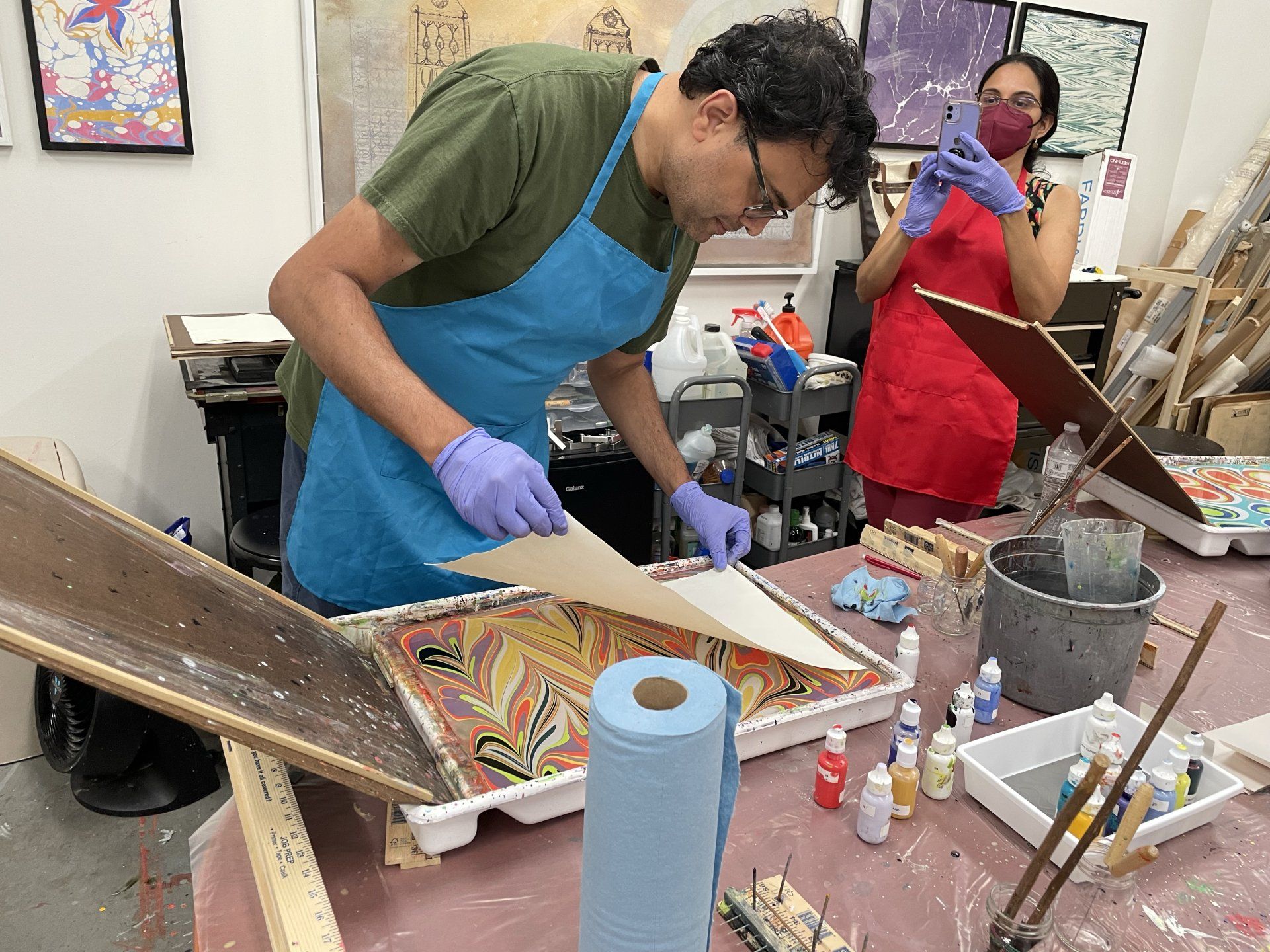 Man begins to carefully lay his paper on the marbling bath as Garubba taught him.