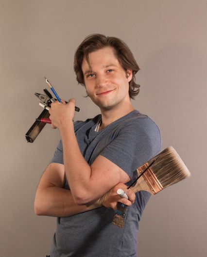 Artist Garubba holds tools of his trade:  brushes, rollers, gouges, and pencils.