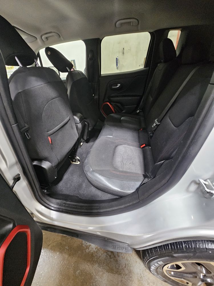 Back seat interior of a silver car with black seats and a red accent; the door is open.