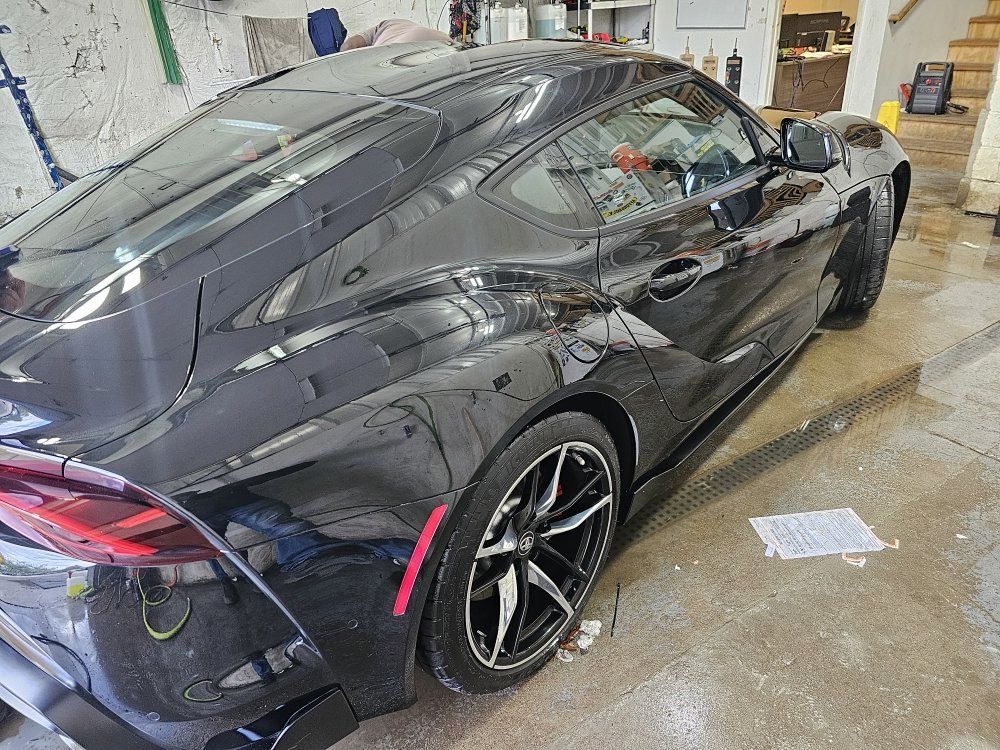 Black Toyota Supra parked indoors, shiny with tinted windows, near tools and equipment.