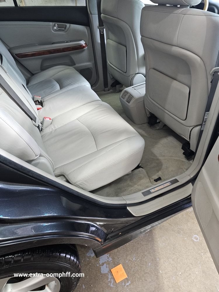 Rear interior of a light-colored Lexus with leather seats and door open, showing back seats and carpet.