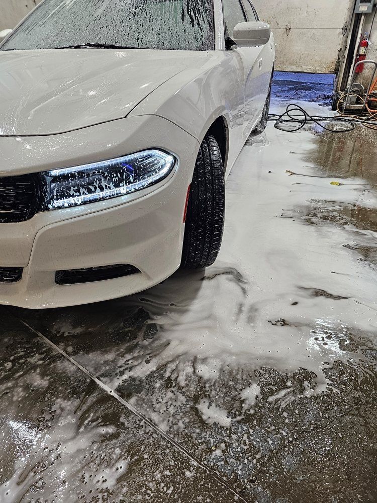 White Dodge Charger being washed, with soapy water on the floor.