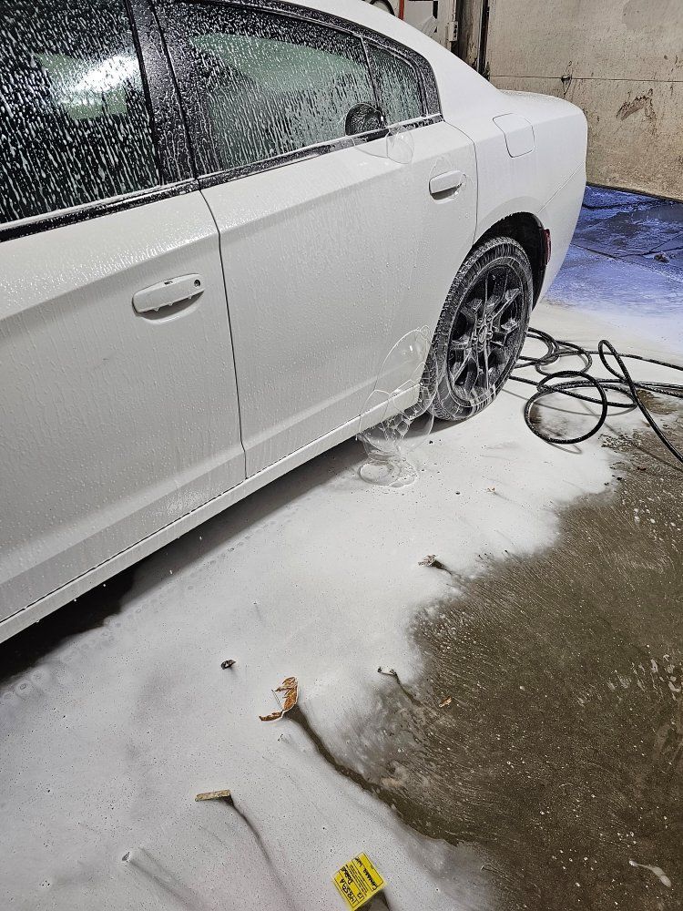 White car being washed with foamy soap at a car wash.