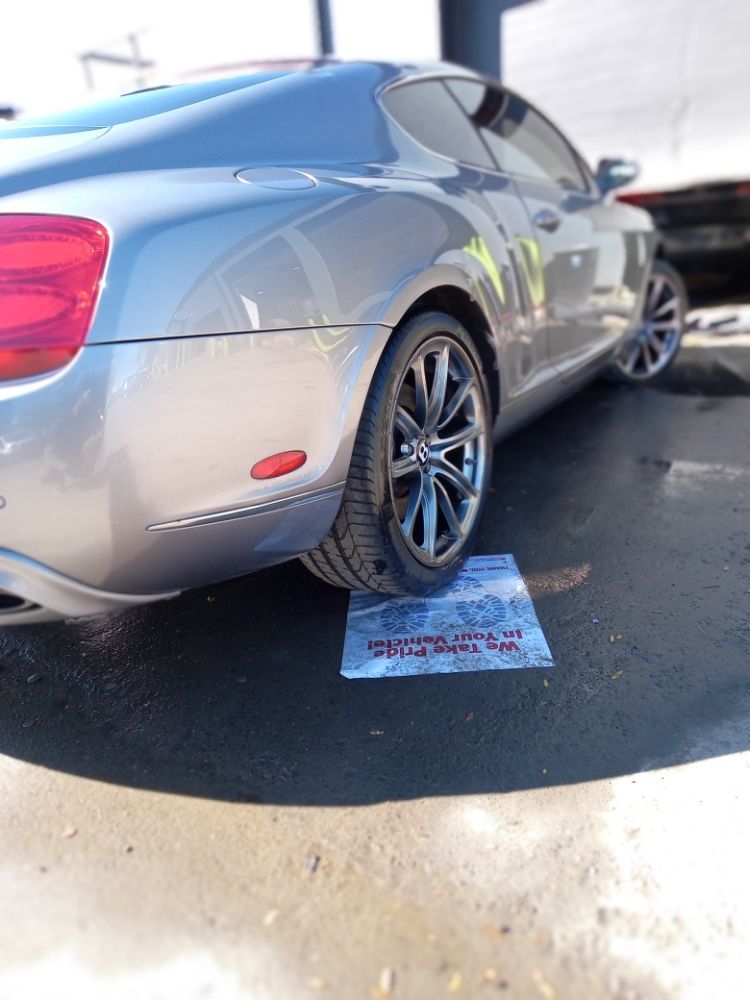Silver Bentley coupe parked on wet pavement at a car wash.