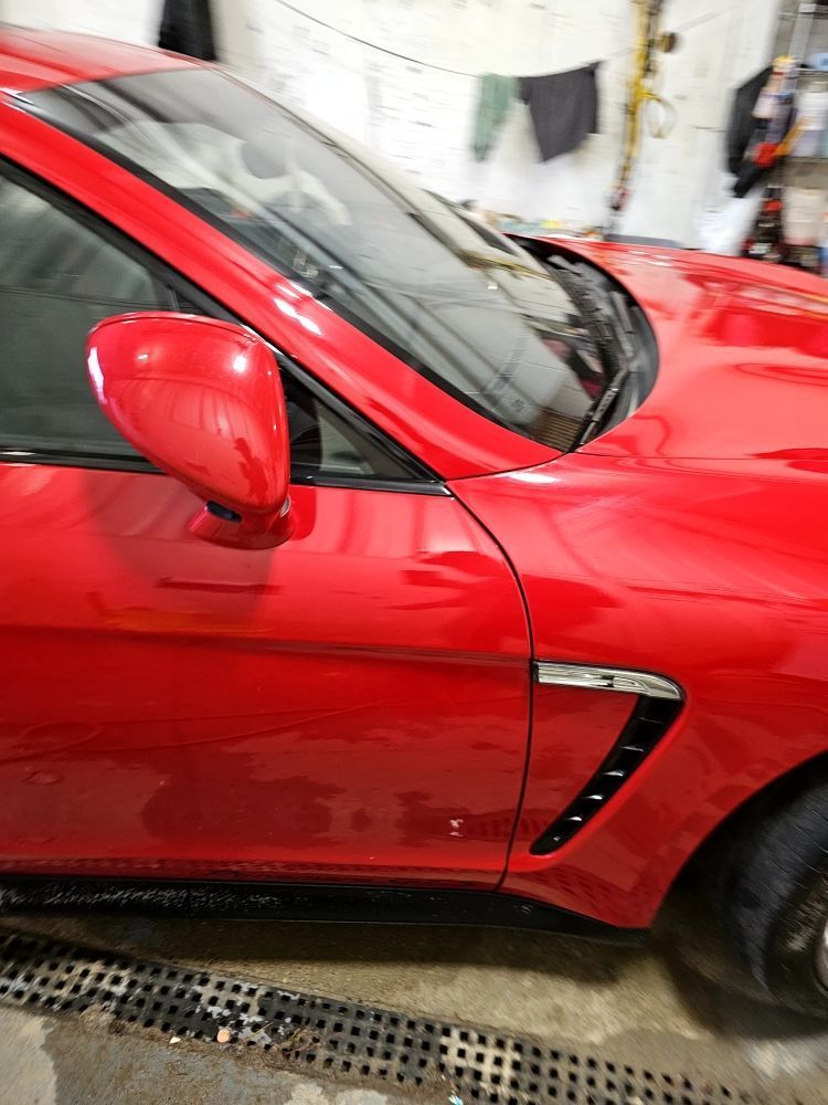 Red sports car side profile, showing mirror and vent. Garage setting.