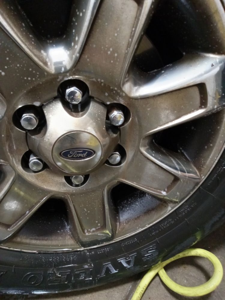 Close-up of a Ford car wheel, with a silver rim, black tire, and Ford logo.
