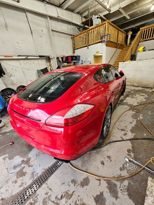 Red Porsche Panamera in a garage with wooden stairs.