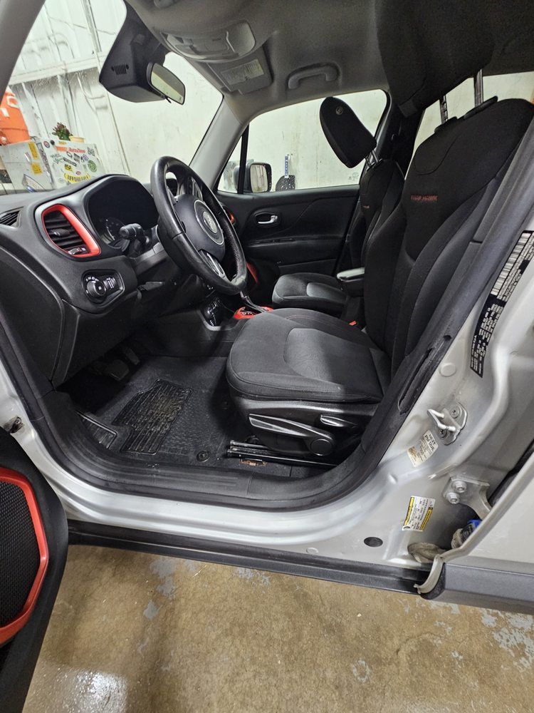 Interior of a silver Jeep Renegade. Black seats, steering wheel, and dashboard with red accents.