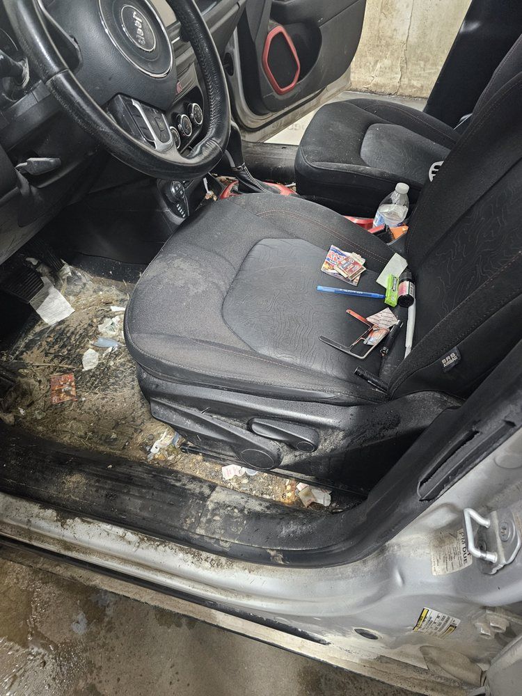 Dirty car interior with trash on floor and seat. Steering wheel on left.
