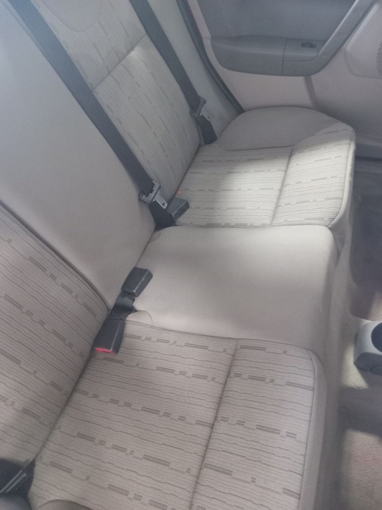 Beige car back seat with patterned fabric and seat belts.