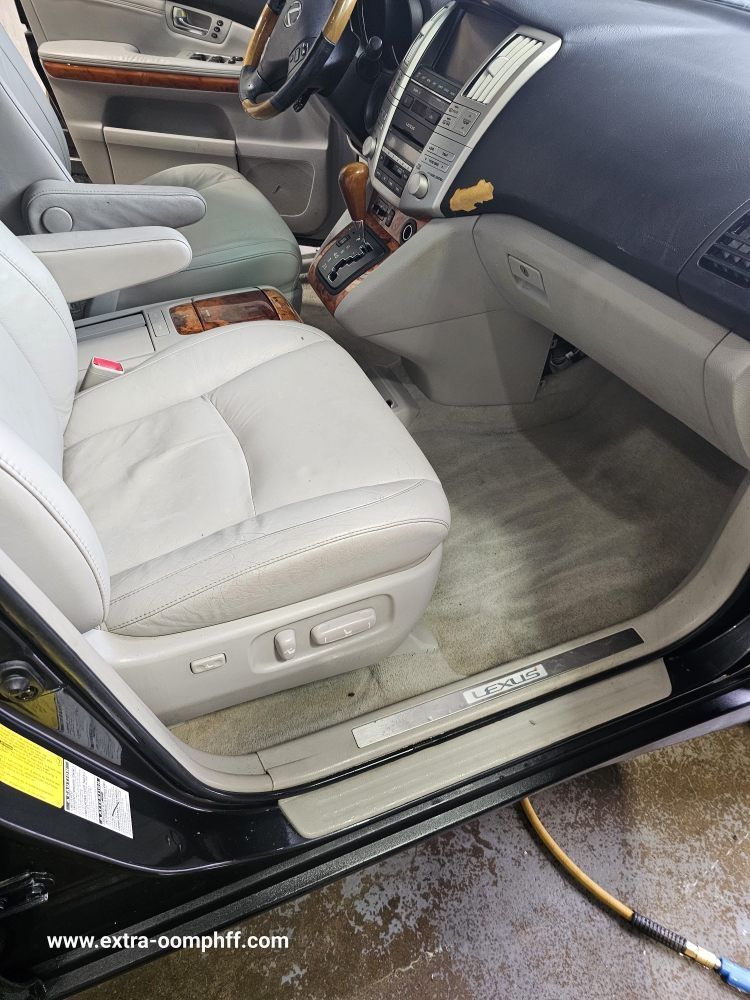 Interior of a light gray Lexus with wood trim, clean seats, and carpet. The door is open.