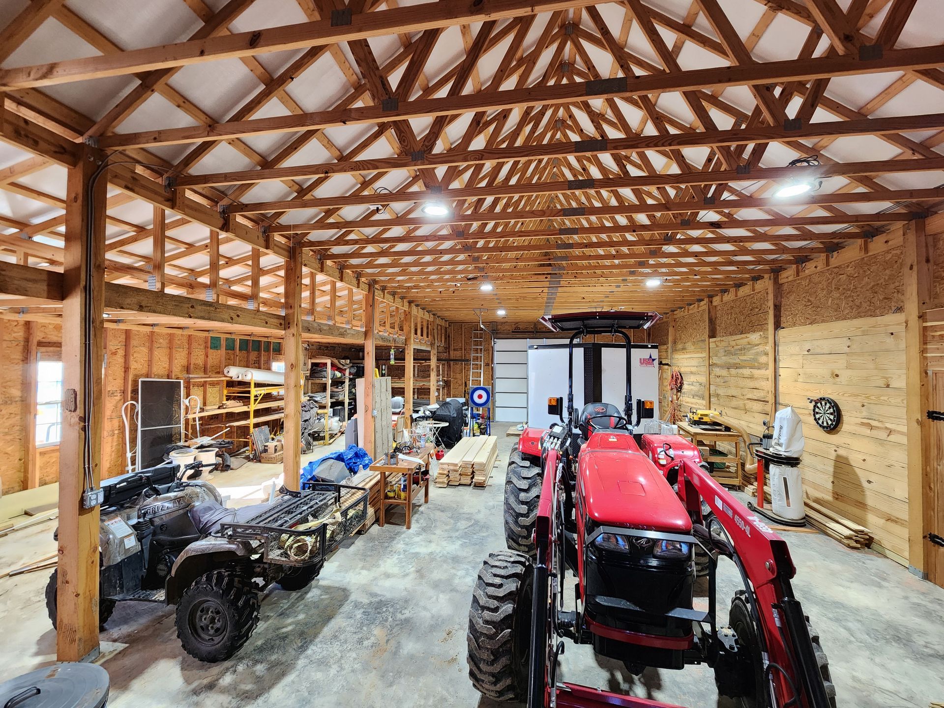 Large wooden barn interior; tractor and ATV parked, tools and storage visible. Bright lighting.