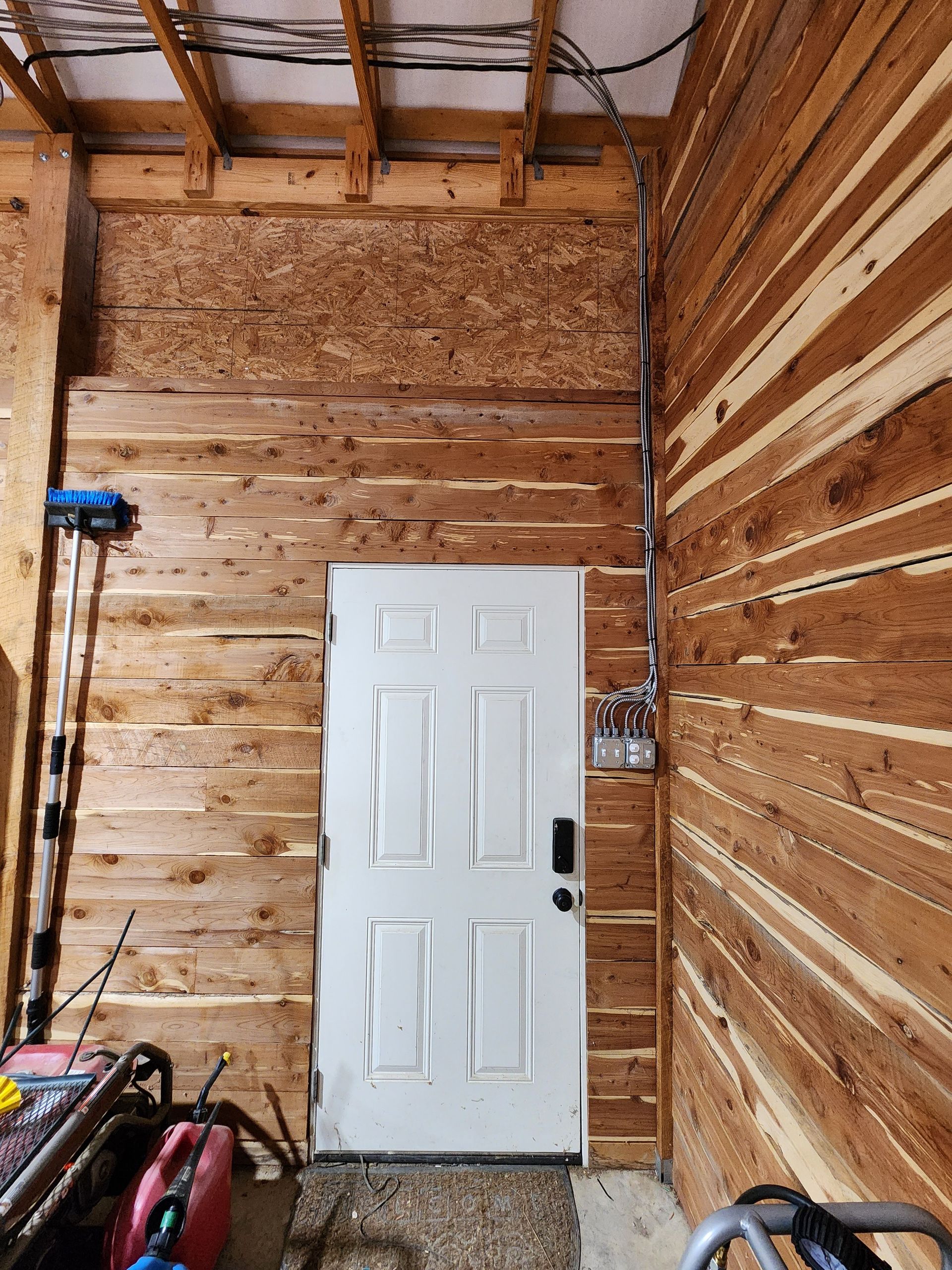 White door set in a wood-paneled wall, with electrical wiring visible.