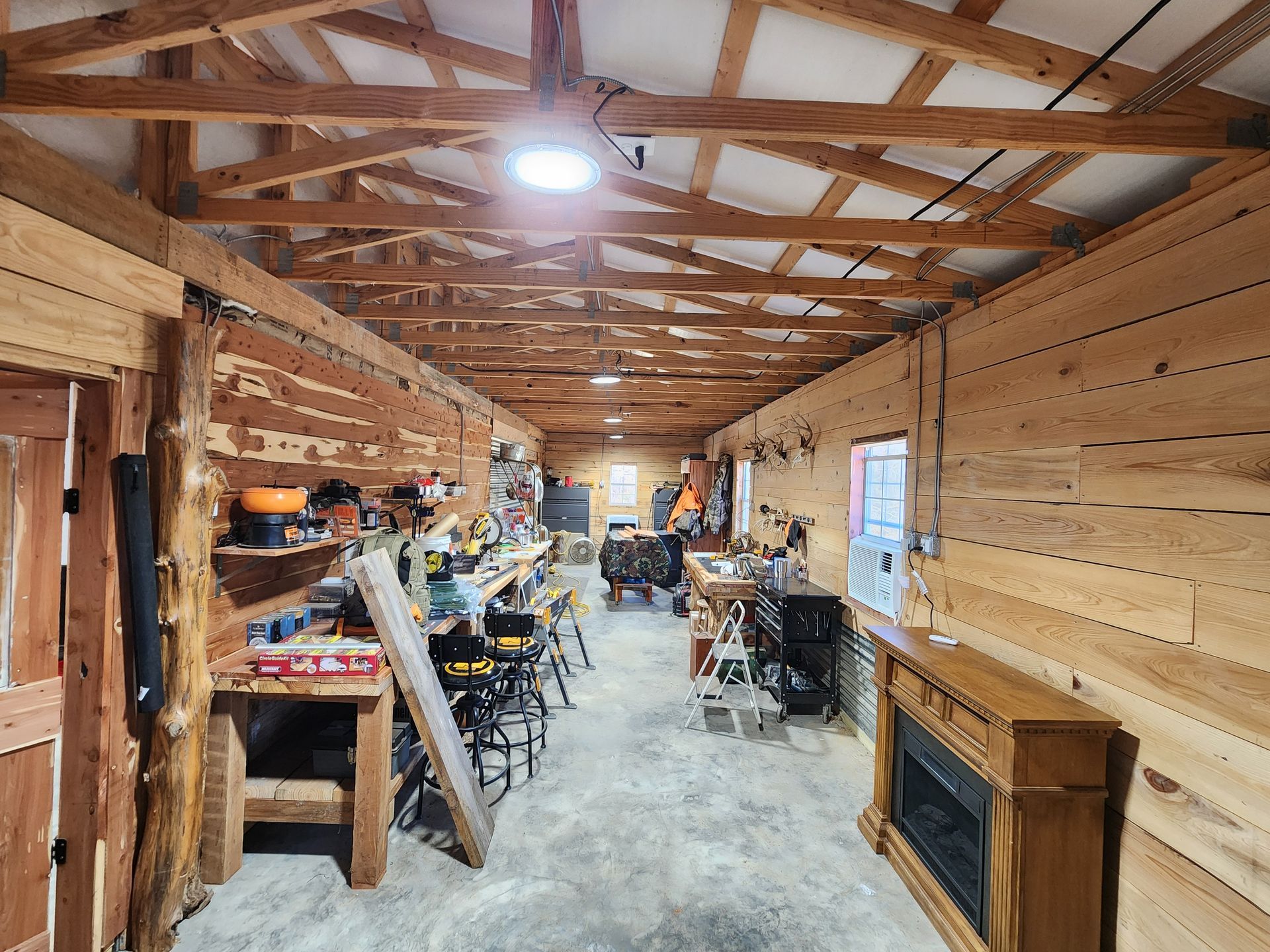 Workshop interior with wooden walls and ceiling, tools on shelves, and a fireplace.