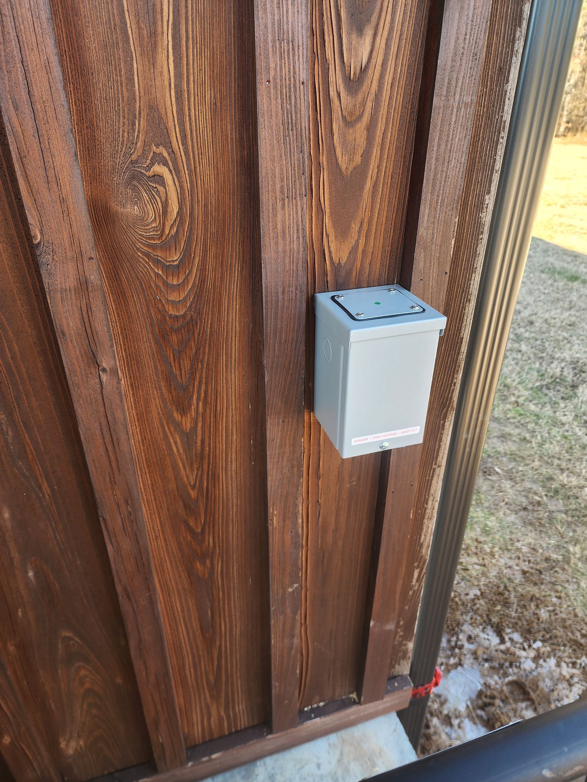 Gray electrical box mounted on a brown wooden wall.
