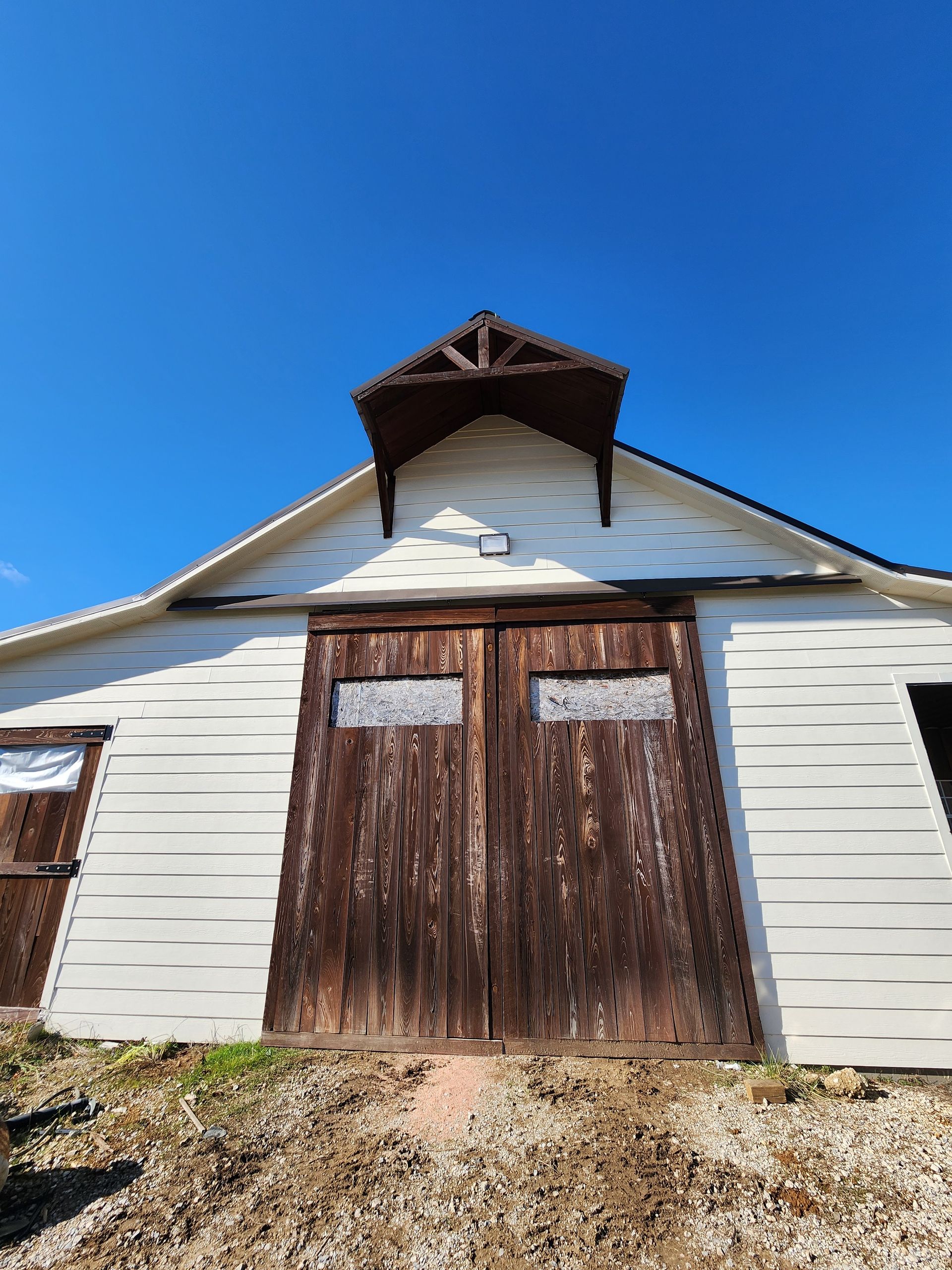 White barn with brown doors and a small decorative roof against a blue sky.