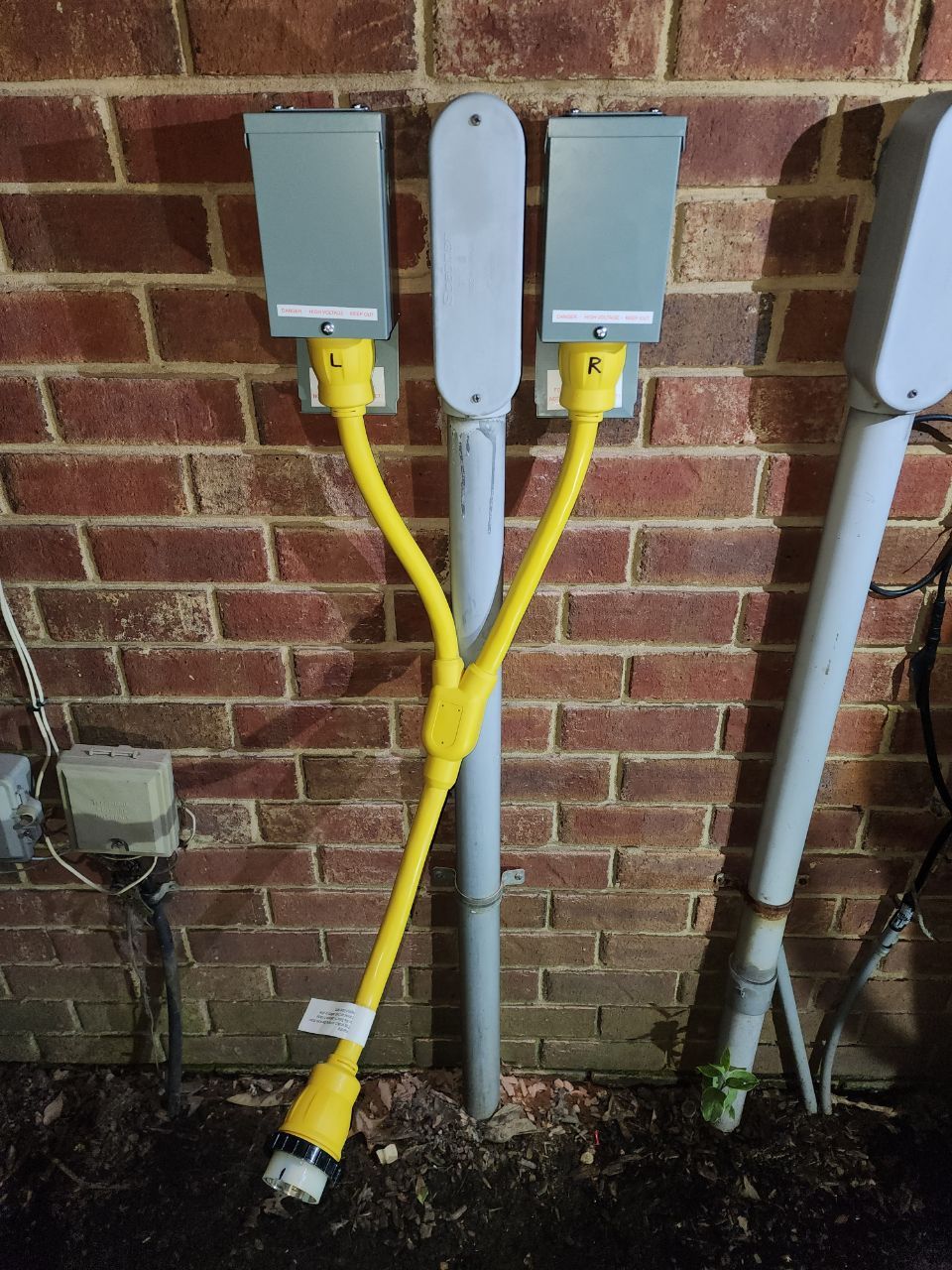 Yellow Y-adapter cord connecting two gray electrical boxes to a single, lower outlet. Brick wall background.