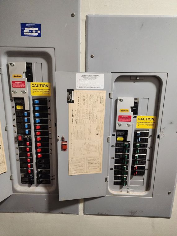 Two open electrical panels with circuit breakers, labels, and wiring in a building.