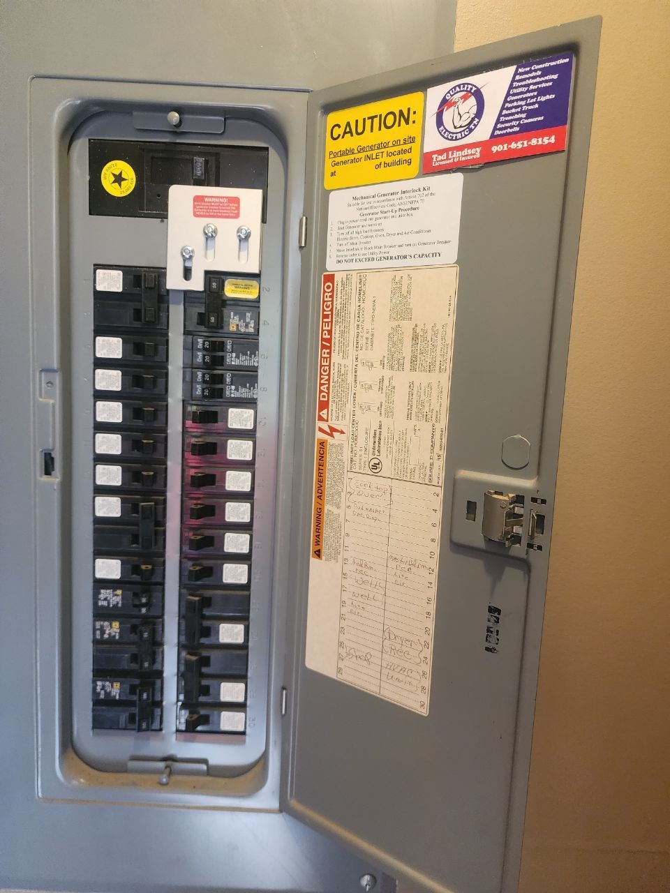 Opened gray electrical panel with circuit breakers, labels on door.