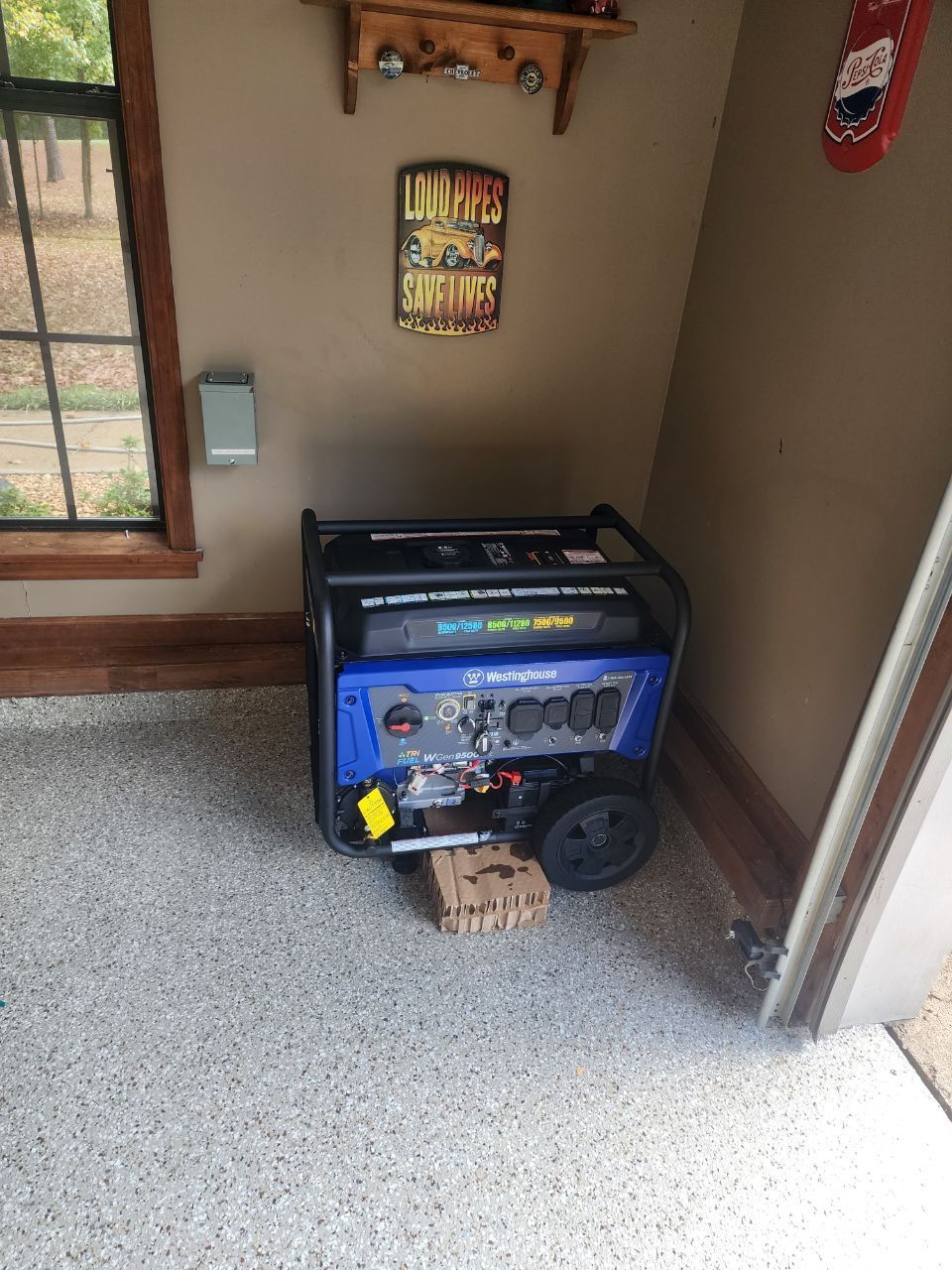 Blue and black portable generator inside a garage next to a window and door.