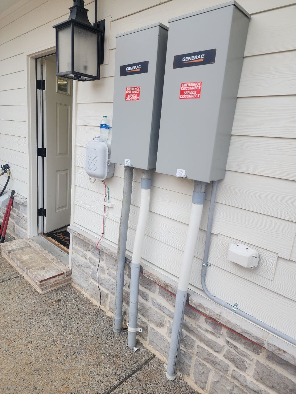 Two gray electrical boxes mounted on a house exterior, with conduit running down to the ground. A front door is visible.
