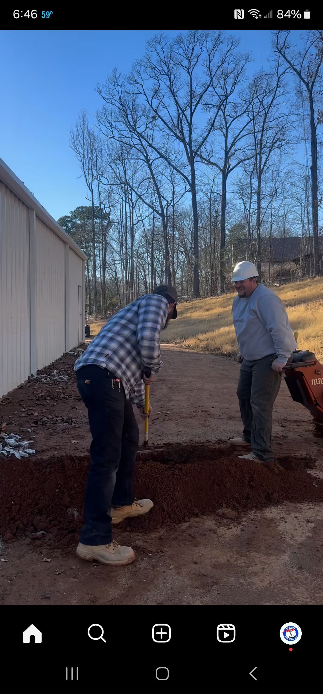 Two men working outdoors, one digging, the other standing with a tiller. The ground is brown, the sky is blue.