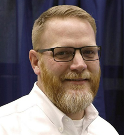 Man with beard and glasses, wearing a white shirt, smiling.