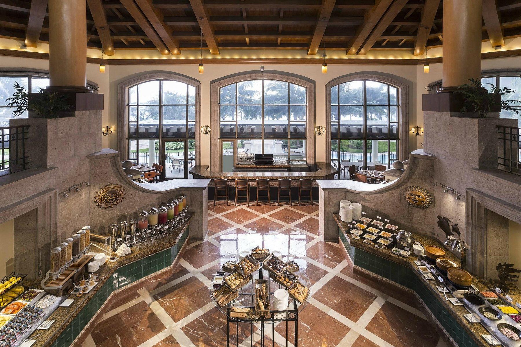 Buffet with food displays in a grand hall, with high windows overlooking water.