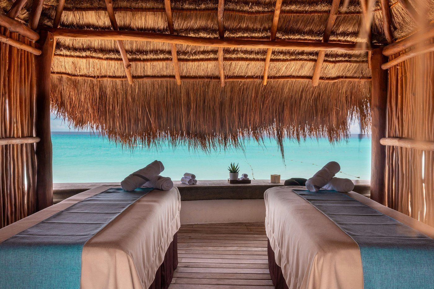 Beachfront spa with two massage tables under a thatched roof, overlooking turquoise water.