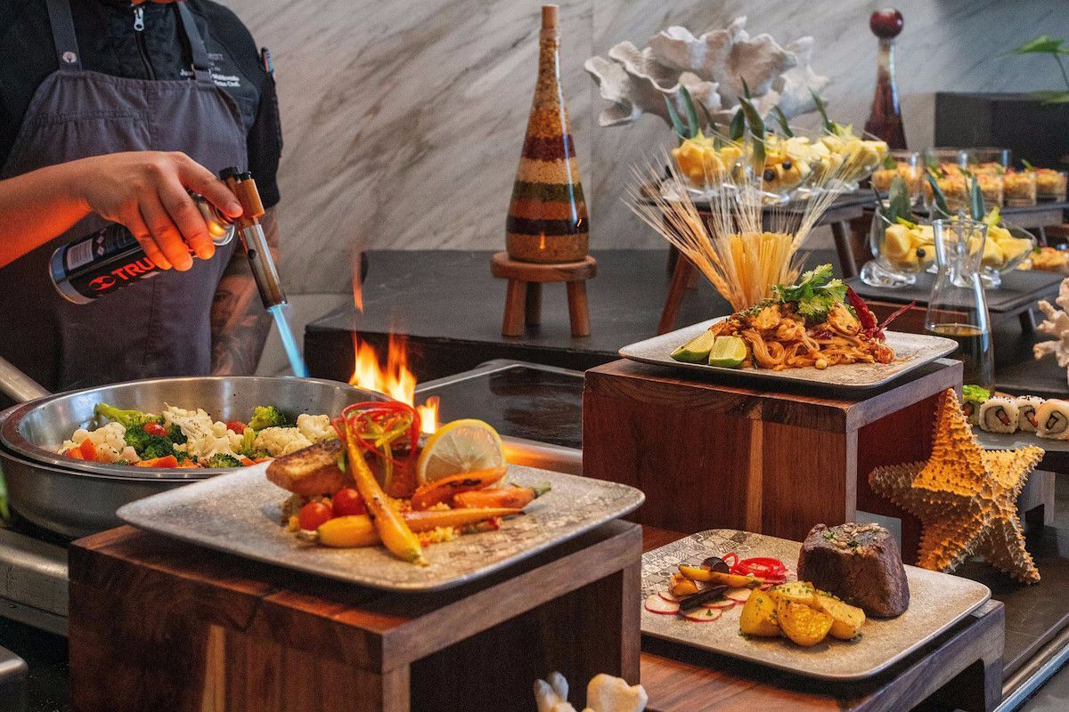 Chef torches dish on buffet table with other food options displayed.