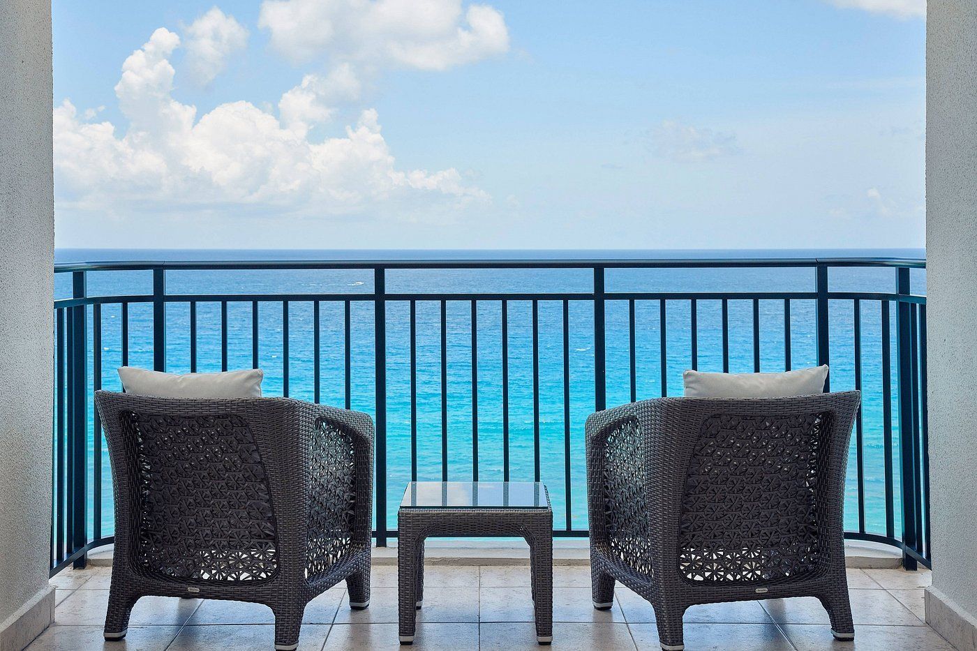Two wicker chairs and small table on a balcony overlooking the ocean.