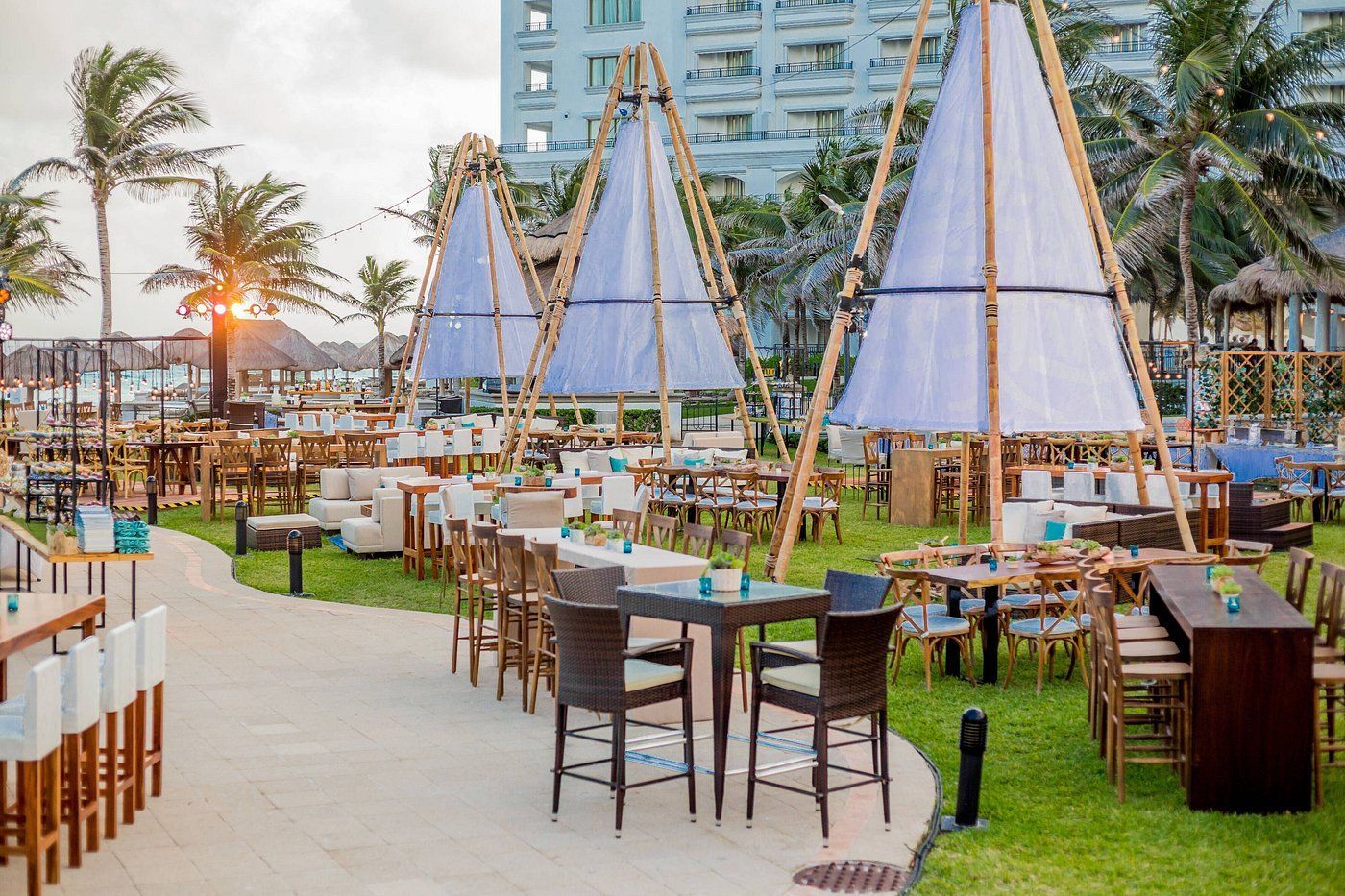 Outdoor event with tables and seating under white canvas structures, near palm trees and a building.
