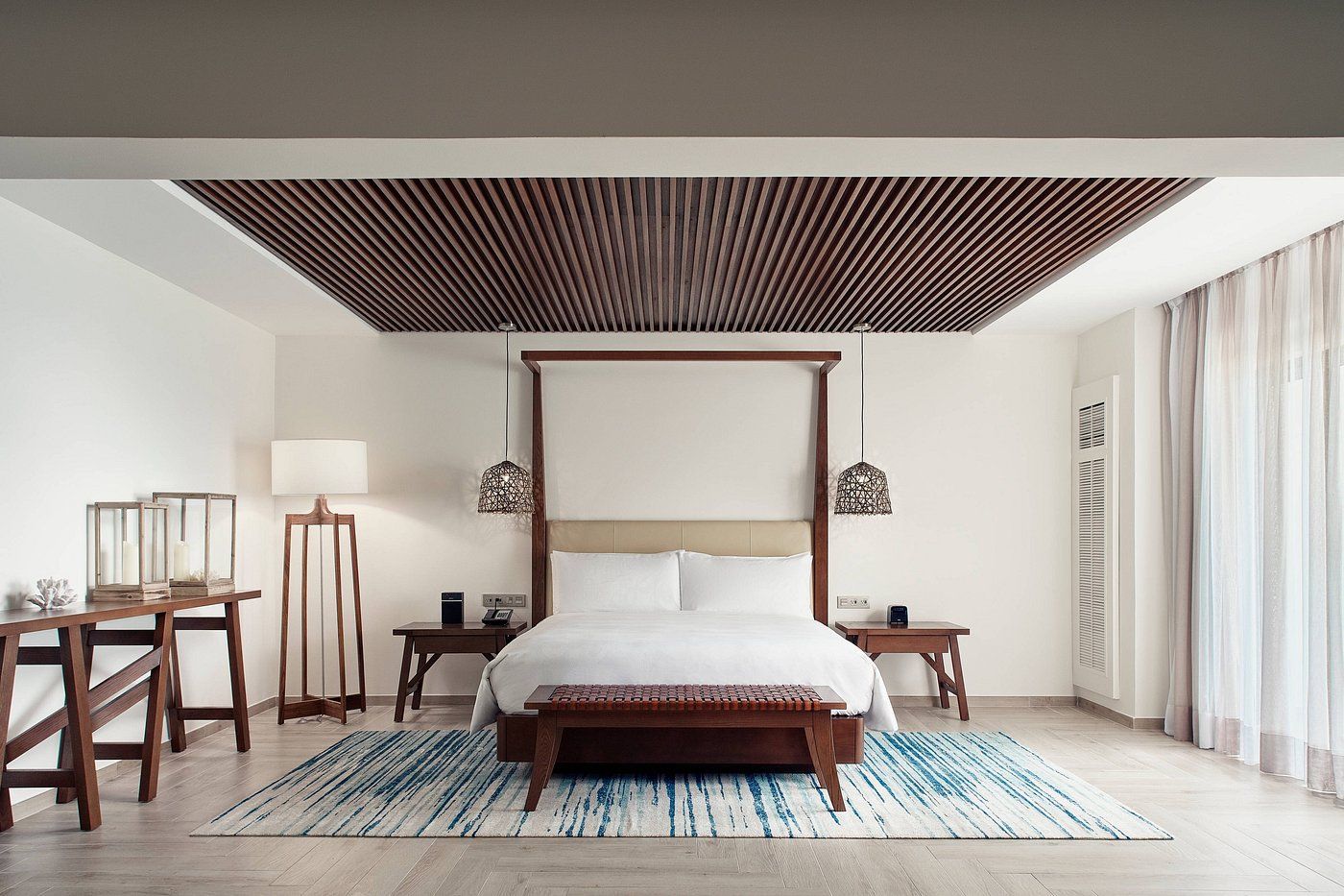 Spacious white bedroom with bed, wooden bench, blue rug, and textured ceiling design.