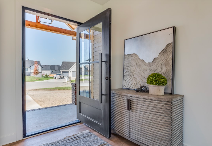 Open black front door reveals neighborhood view, with a gray console table inside; artwork and plant on top.