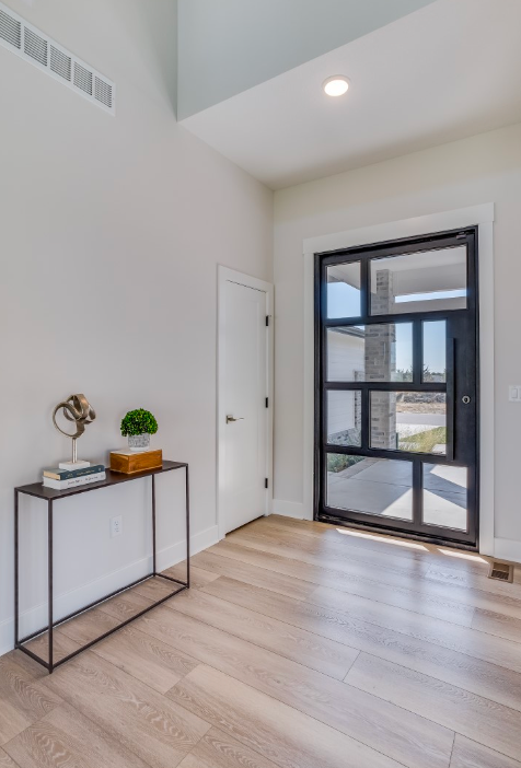 Interior shot of a modern entryway with light wood flooring, a black-framed glass door, and a console table with decor.