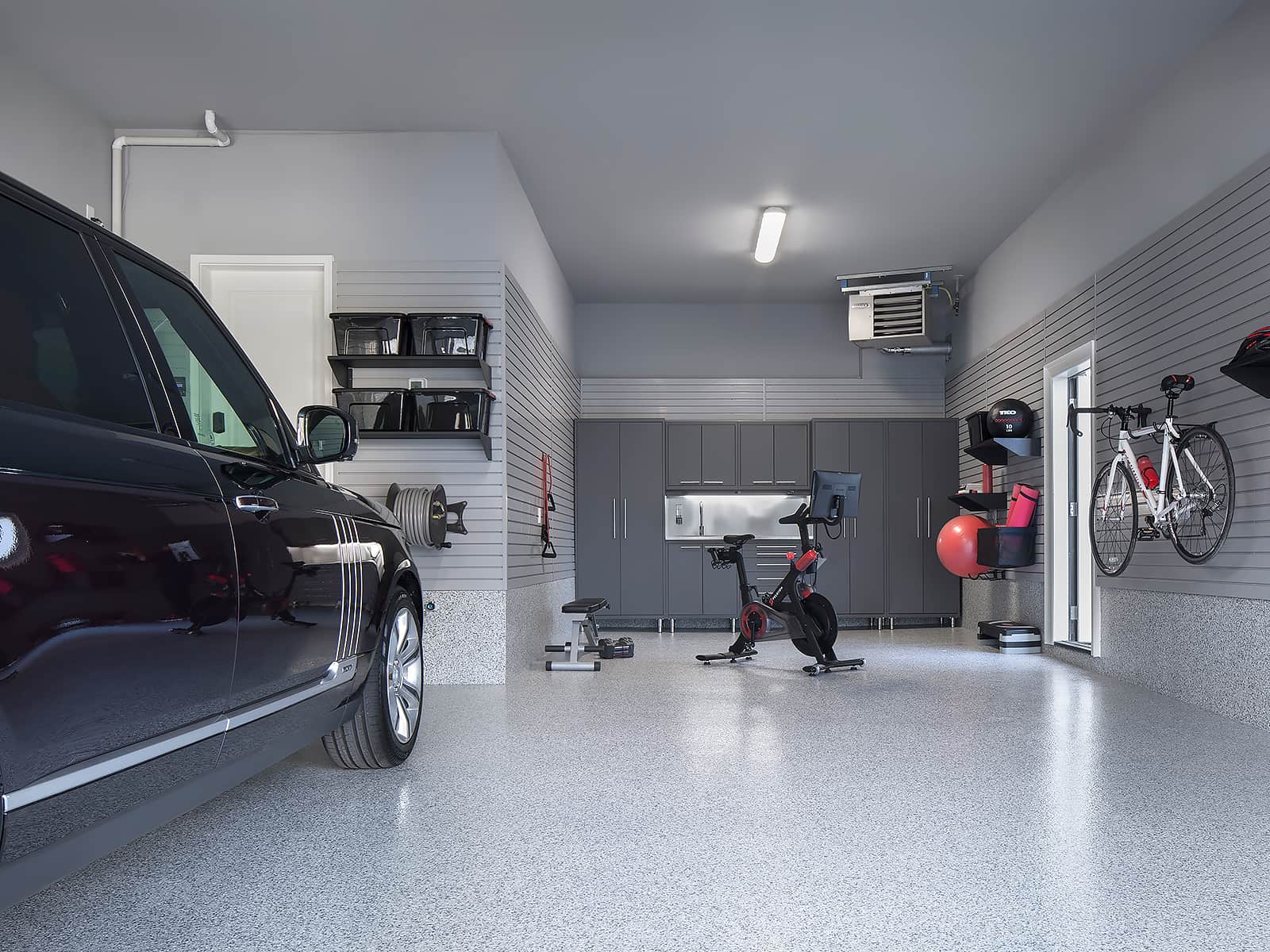 A modern garage with a parked car, workout equipment, and storage, featuring gray walls and a speckled floor.