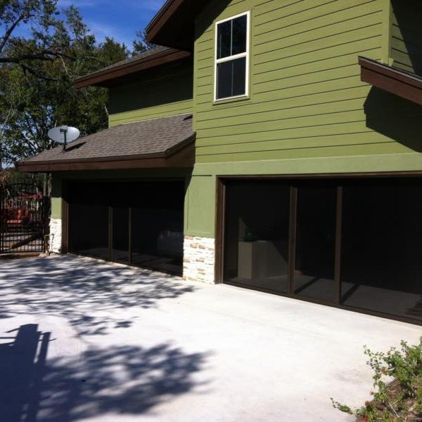 Two-story green house with garage. Dark screen garage doors, white concrete driveway, and satellite dish.