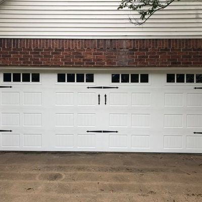 White garage door with black decorative hardware; above, a brick section and light siding.